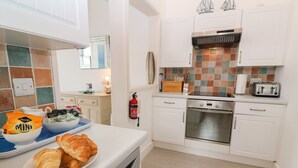 A modern kitchen with white cabinets, a stainless steel oven, and a tiled backsplash. - Beachcomber (Marazion)