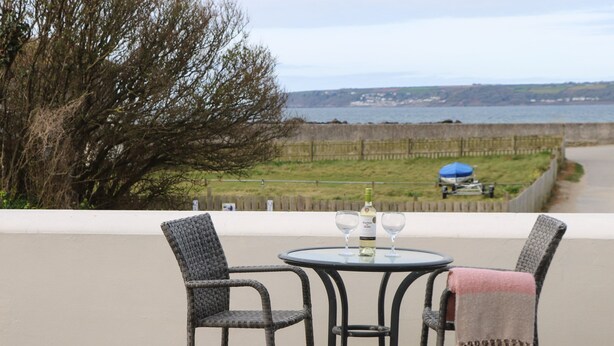 A table with two chairs and a bottle of wine on a balcony overlooking a body of water. - Beachcomber (Marazion)