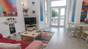 A modern living room with a TV, fireplace, and dining area. - Beachcomber (Marazion)