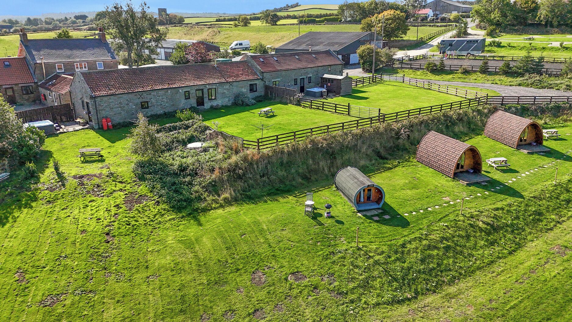 A rural property with stone buildings, a fenced lawn, and several small wooden structures.