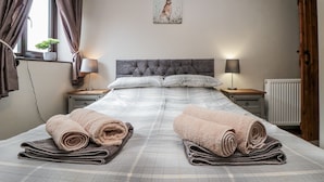 A neatly made bed with two rolled towels, a grey headboard, bedside lamps, a window with curtains, and a painting of a rabbit on the wall. - Carters (Scarborough)