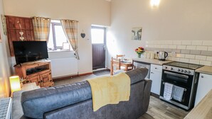 A compact living space with a sofa, a television, a dining table, and a kitchen area including an oven and a kettle. - Carters (Scarborough)