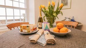Une table à manger avec une bouteille de Prosecco, un vase rempli de tulipes jaunes, une assiette d’oranges et une boîte de gâteau au chocolat de la marque M&S.