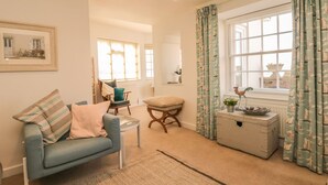 Un salon chaleureux avec un canapé bleu, une chaise en bois, une petite table et une fenêtre avec des rideaux.