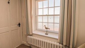 Une pièce avec une fenêtre donnant sur une plage, un radiateur en dessous et une porte avec une poignée.