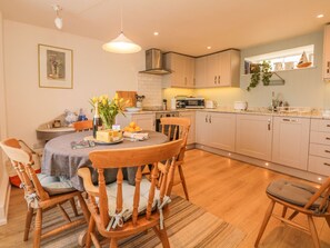 A modern kitchen with wooden cabinets, a dining table with chairs, and a hanging light fixture. - Searles (Exmouth)