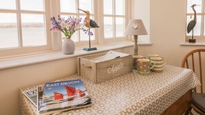 Une chambre avec vue sur la mer, une table en bois sur laquelle est posée une carte, une lampe et des objets de décoration, dont une sculpture d’oiseau.