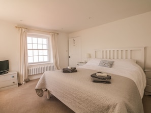 A bedroom with a bed, a nightstand, a dresser, a window with curtains, and a radiator. - Searles (Exmouth)