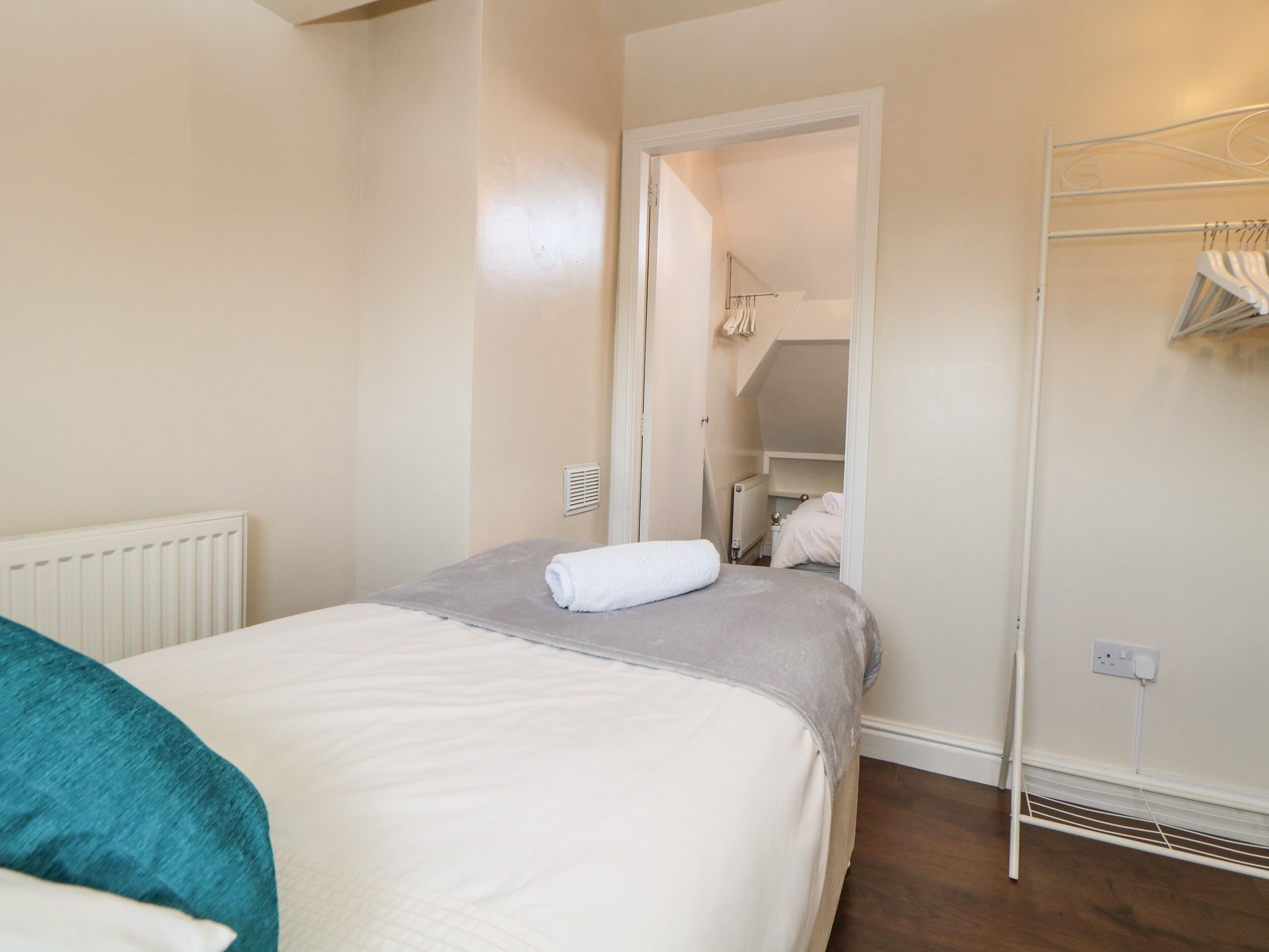 A bedroom with a bed, a radiator, a wardrobe, and a hanging clothes rack.