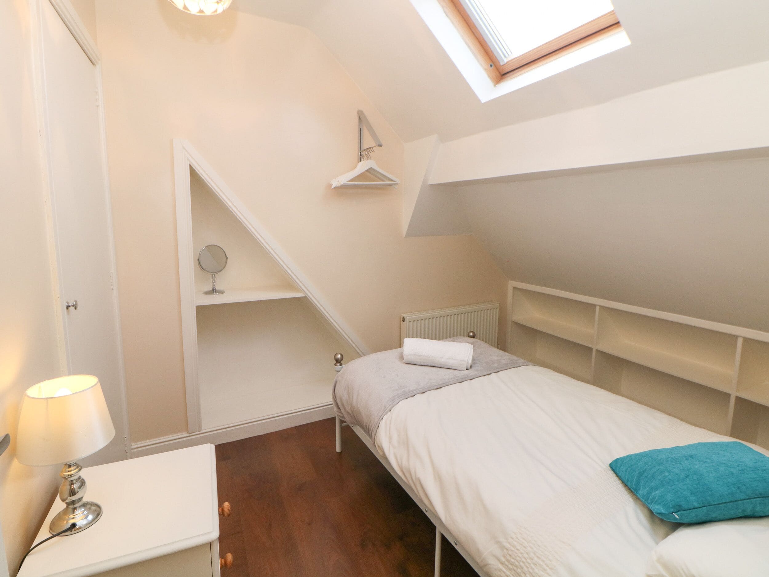 A bedroom with a bed, a bedside table with a lamp, a hanging light fixture, a radiator, and a skylight.
