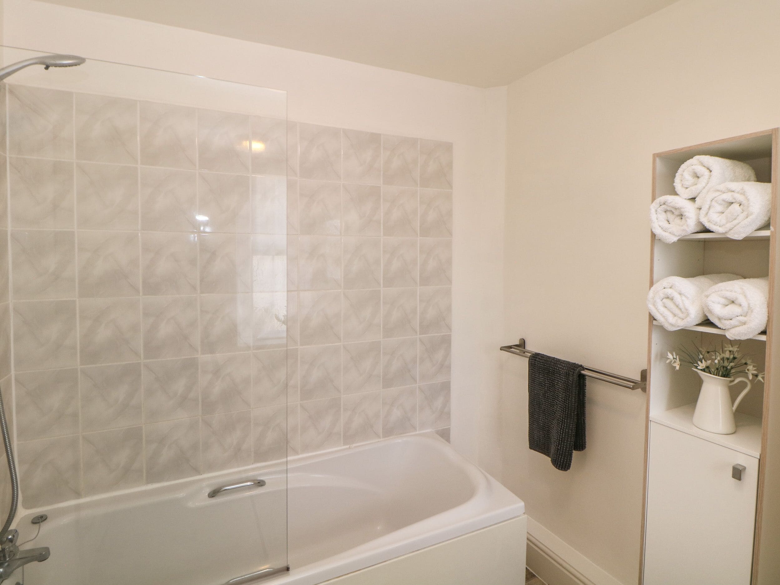A bathroom with a glass-enclosed shower, a white bathtub, and a towel rack with neatly folded towels.