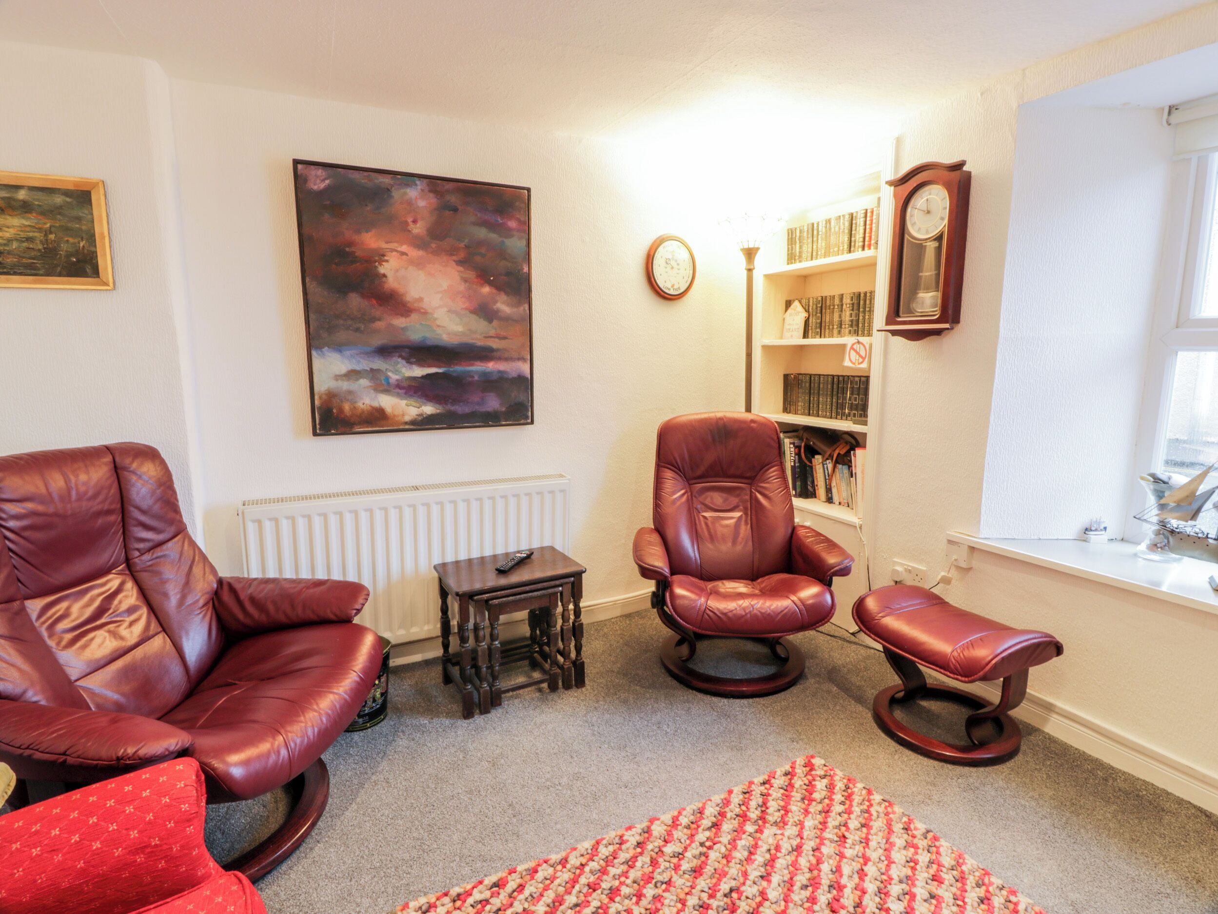 A living room with leather chairs, a small table, a bookshelf, and a painting on the wall.