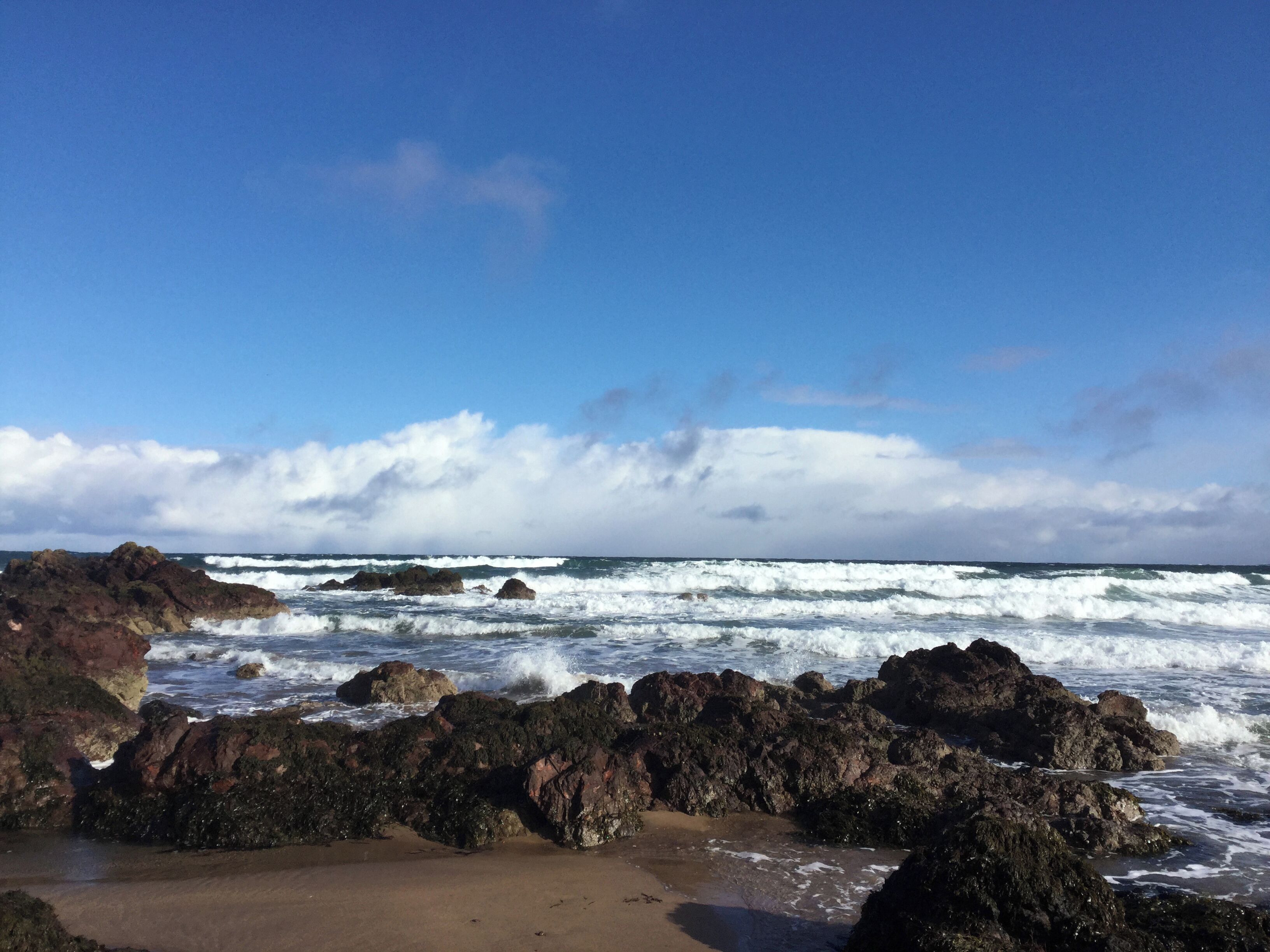 A rocky beach with waves crashing against the shore under a clear sky.