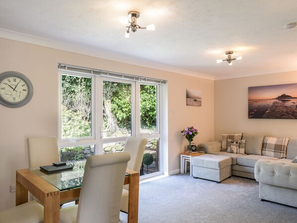 Relax in this inviting living room with a sofa, dining table, and window offering a view of lush greenery.