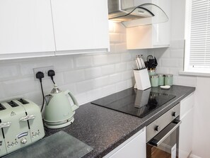 A modern kitchen with white cabinets, a black countertop, a kettle, a toaster, and a coffee maker. - Little Retreat (Liskeard)