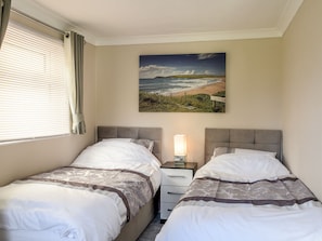 Two single beds with grey headboards and white bedding, a bedside table with a lamp, and a large landscape painting adorn this serene hotel room.
