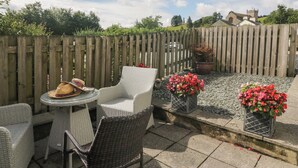 A patio with wicker furniture, a round glass table, and potted plants. - Betty's Mews (Ambleside)