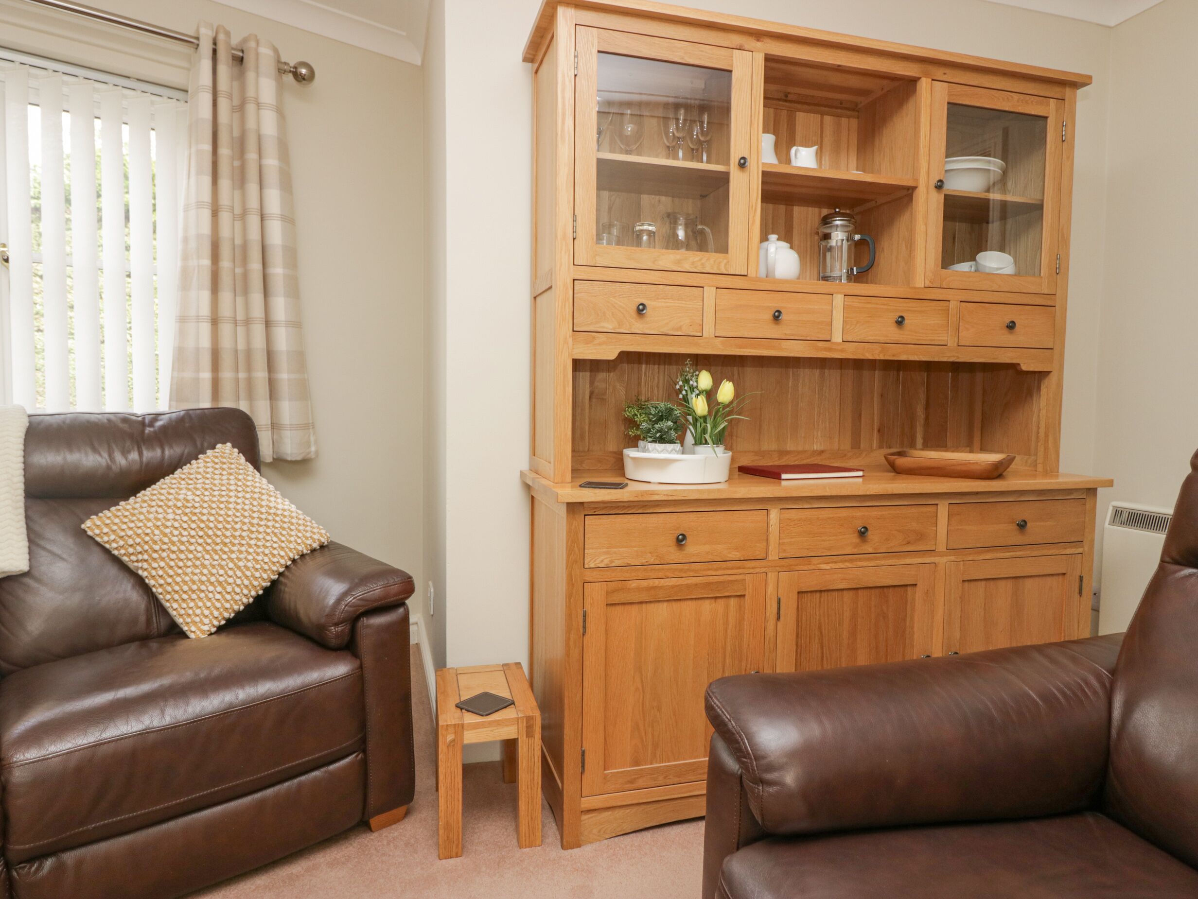 A living room with two brown leather sofas, a wooden cabinet with glass doors, and a small wooden side table.