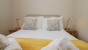 A neatly made bed with white linens and two decorative pillows, a yellow blanket, and two bedside lamps on wooden nightstands. - Betty's Mews (Ambleside)