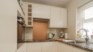 A modern kitchen with white cabinets, a granite countertop, a built-in oven, and a window with blinds. - Betty's Mews (Ambleside)