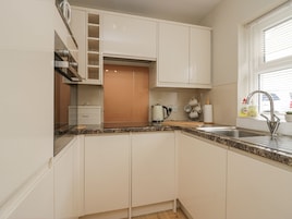 Una cocina moderna con armarios blancos, encimera de granito, horno empotrado y ventana con persianas.