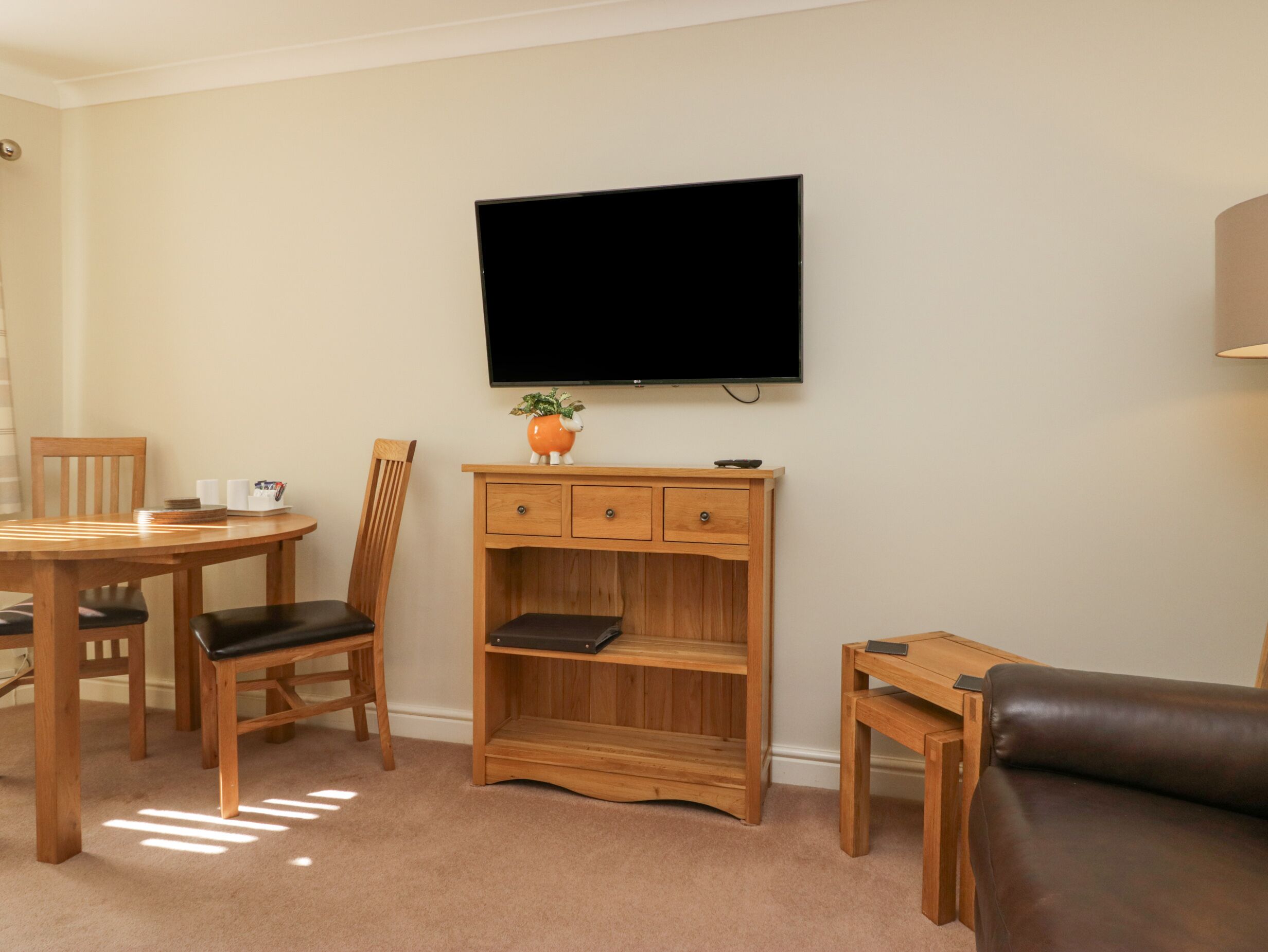 A living room with a wooden TV stand, a flat-screen TV, a dining table with chairs, and a leather sofa.