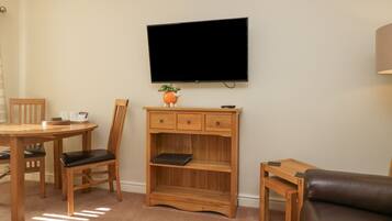 A living room with a wooden TV stand, a flat-screen TV, a dining table with chairs, and a leather sofa.