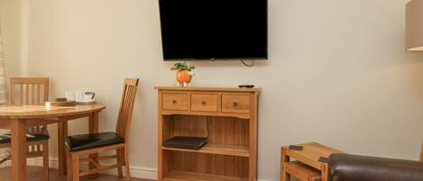 A living room with a wooden TV stand, a flat-screen TV, a dining table with chairs, and a leather sofa.