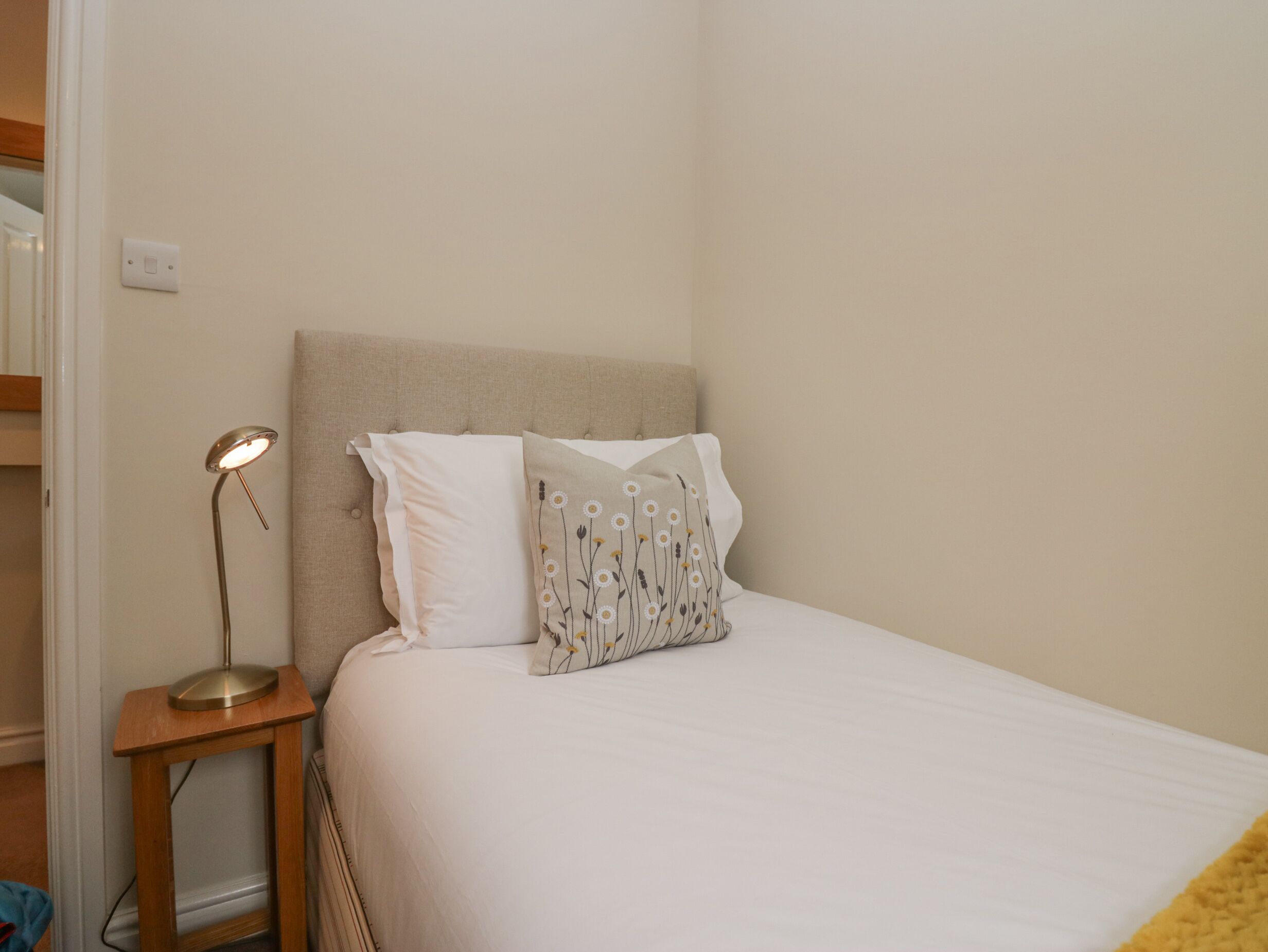Un lit bien fait, avec une literie blanche et deux coussins décoratifs, une lampe de chevet et une petite table de nuit en bois.