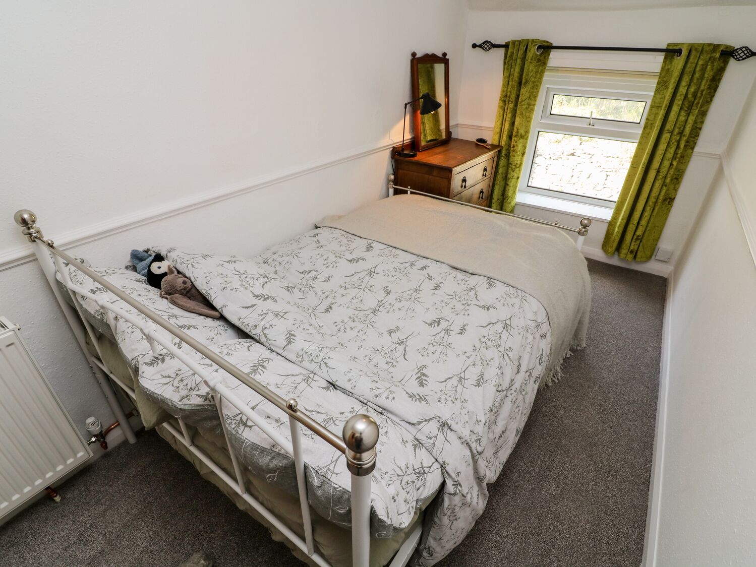 Ein Schlafzimmer mit einem Einzelbett, einem Schminktisch, einem Spiegel und einem Fenster mit Vorhängen.
