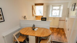 Cocina compacta con una mesa de madera, armarios blancos y una ventana.