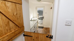 Vista a través de una puerta de madera que da a una cocina con un lavabo y una lavadora.