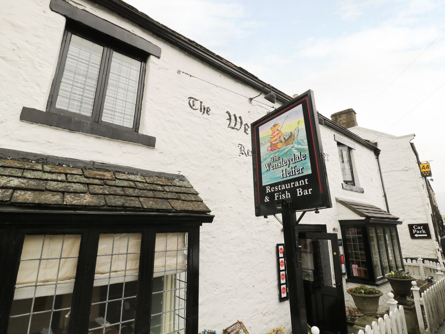 A white building with a sign for The Wensleydale Heifer Restaurant & Fish Bar.