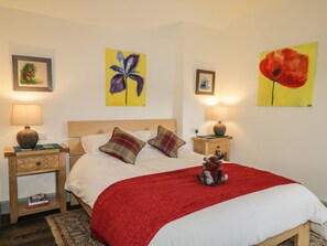 Un lit bien fait, recouvert d’une couverture rouge, deux tables de chevet avec des lampes et trois tableaux accrochés aux murs.
