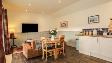 Una sala de estar acogedora con un sofá, una mesa de comedor con sillas, un televisor montado en la pared y una zona de cocina con armarios y una encimera.