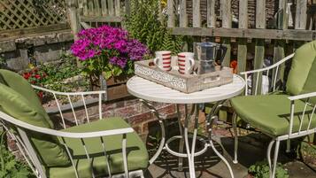 A patio with two white metal chairs and a table, surrounded by a wooden fence and potted plants.