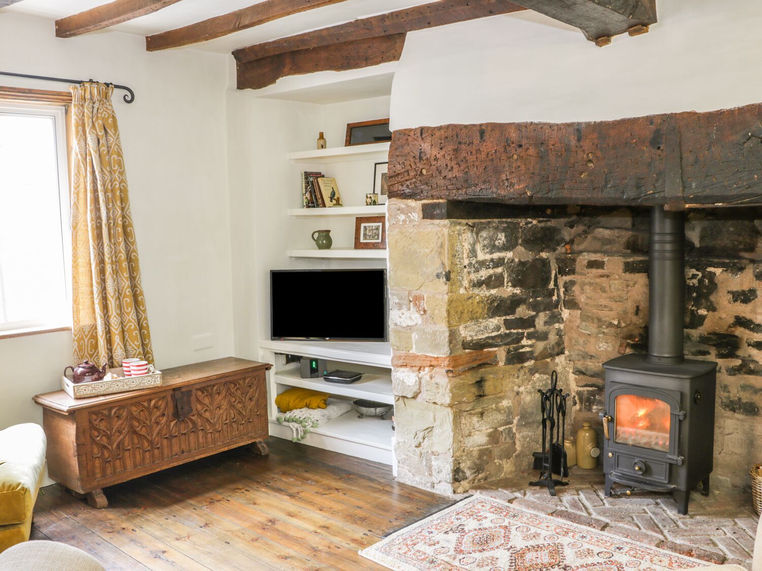 A cozy living room with a stone fireplace, wooden furniture, and a television on a shelf.