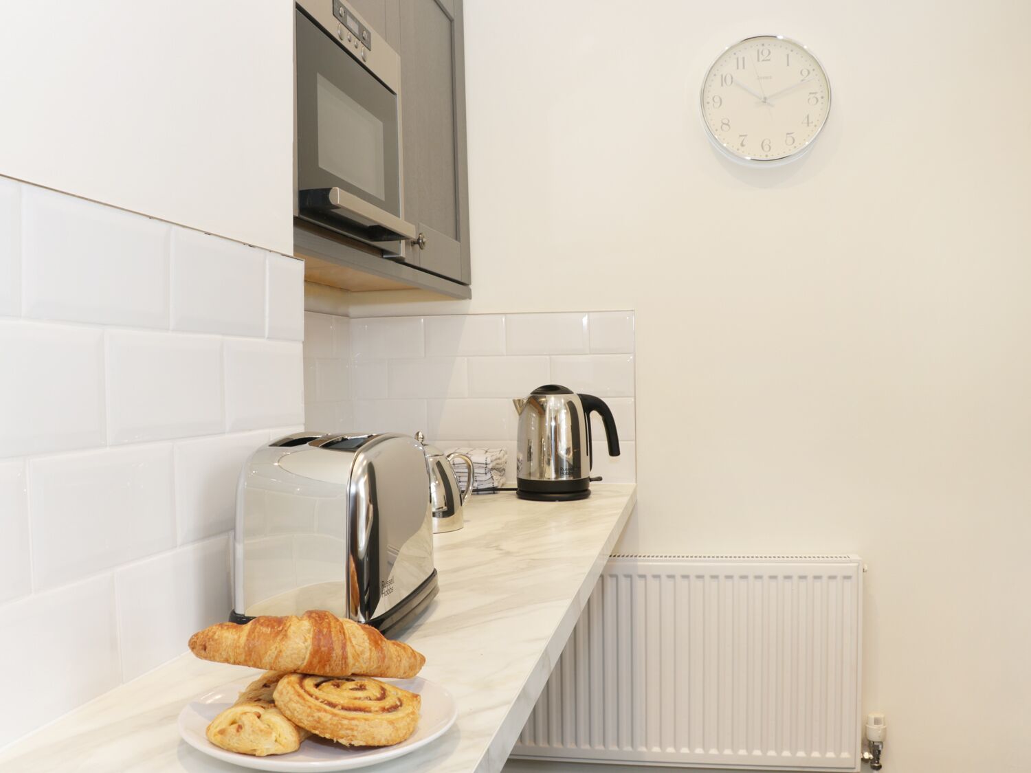 A kitchen with a toaster, kettle, and croissants on the counter.