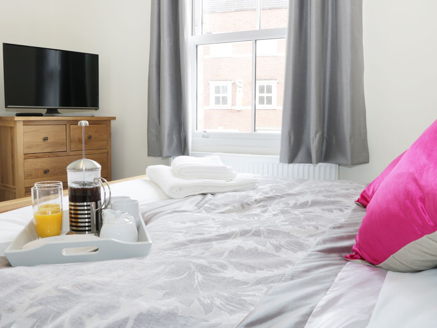 Hotelkamer met een bed, een televisie, een ontbijttafel met jus d'orange, een koffiezetapparaat en een raam met gordijnen.