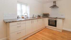 A modern kitchen with white cabinets, a granite countertop, a built-in oven, and a window with blinds. - Granary 1 (Hereford)