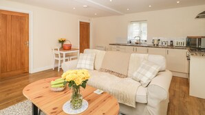 A modern living room with a wooden coffee table, a white sofa, and a kitchen area with a microwave and toaster. - Granary 1 (Hereford)