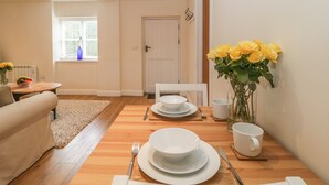 A dining area with a wooden table set for four, a white door, and a vase of yellow roses on the wall. - Granary 1 (Hereford)