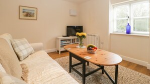 A living room with a sofa, a coffee table with fruit, a TV, and a window with blinds. - Granary 1 (Hereford)