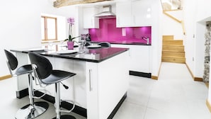 A modern kitchen with white cabinets, a central island with bar stools, a pink backsplash, and a wooden staircase. - Tyddyn Isa (Denbigh)
