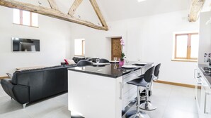 A modern kitchen with a central island, bar stools, and a dining area. - Tyddyn Isa (Denbigh)
