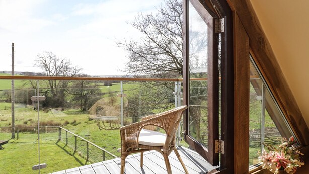 A balcony with a wicker chair and a vase of flowers. - Tyddyn Isa (Denbigh)