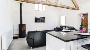 A modern kitchen with a central island, a black sofa, and a TV mounted on the wall. - Tyddyn Isa (Denbigh)