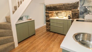 Eine Küche mit einer Wand aus Naturstein, einem Edelstahl-Spülbecken und einer Treppe mit beige bezogenen Stufen.