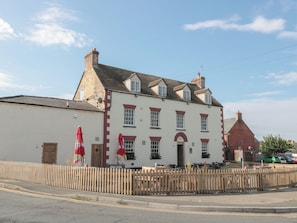 A two-story building with a white facade and red accents, featuring a traditional architectural style with a pitched roof and multiple chimneys. - 1 Westcroft Cottage (Stonehouse)