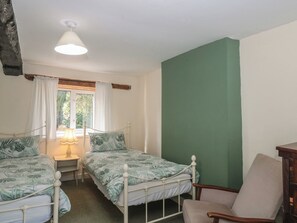 A bedroom with two single beds, a chair, a table with a lamp, and a window with curtains. - 1 Westcroft Cottage (Stonehouse)